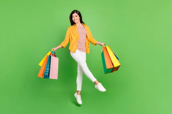 Foto de adorable joven bonita vestida ropa casual sosteniendo bolsas de compras caminando aislado color verde fondo —  Fotos de Stock