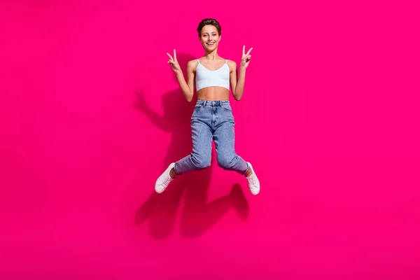 Πλήρες μήκος του σώματος μέγεθος άποψη του αρκετά χαρούμενο κορίτσι άλμα δείχνει v-σημάδι απομονώνονται σε φωτεινό ροζ φόντο χρώμα ματζέντα — Φωτογραφία Αρχείου
