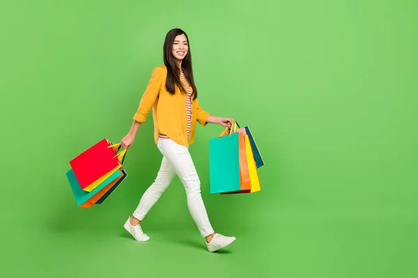 Foto van schattige charmante jonge dame dragen geel shirt glimlachen holding koopjes lopen lege ruimte geïsoleerde groene kleur achtergrond — Stockfoto