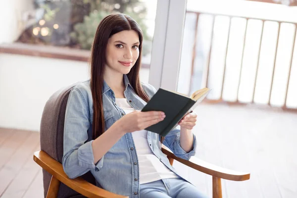 Çekici, neşeli, genç bir kadın. Oturduğu yerden kitap okuyor. Ev içinde iyi ruh hali. — Stok fotoğraf