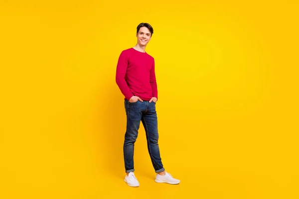 フル長いです写真の優しいブルネット若い男スタンド身に着けている赤いセータージーンズ隔離された黄色の色の背景 — ストック写真