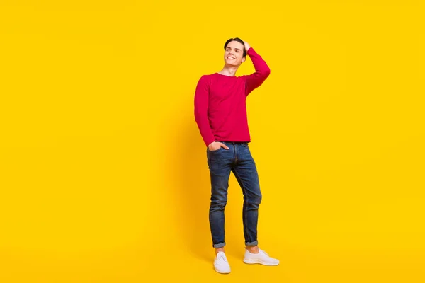 Teljes méretű fotó szép barna Y-generációs srác állni néz üres tér viselni piros pulóver farmer elszigetelt sárga színű háttér — Stock Fotó