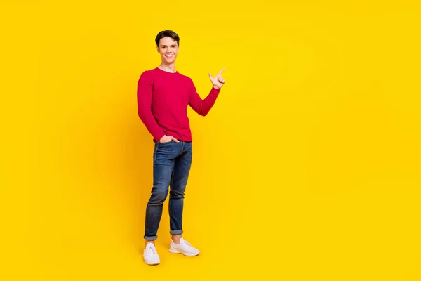 Full storlek foto av optimistiska brunett tusenårig kille punkt tomt utrymme bära röd tröja jeans isolerad på gul färg bakgrund — Stockfoto
