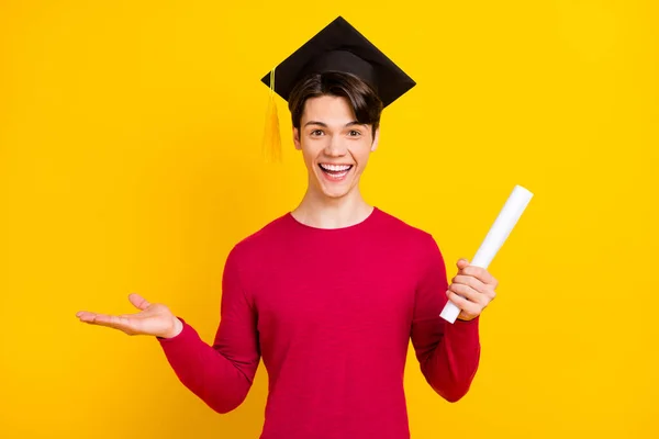 Fénykép boldog csinos srác öltözött piros pulóver agglegény fejfedő gazdaság diploma kar üres tér elszigetelt sárga színű háttér — Stock Fotó