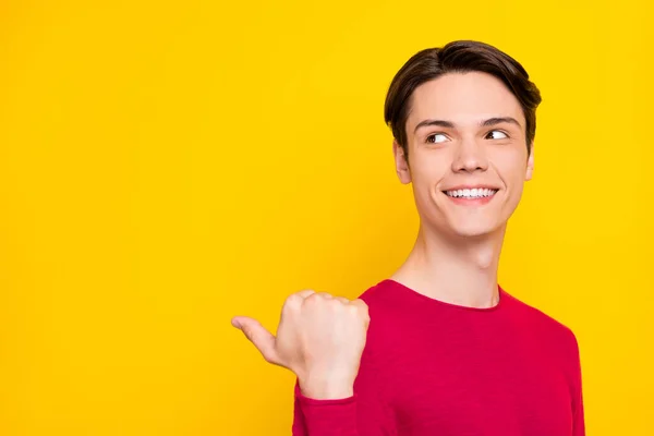 Foto van aantrekkelijke mooie jonge man gekleed rode trui glimlachen wijzende vinger terug lege ruimte geïsoleerde gele kleur achtergrond — Stockfoto