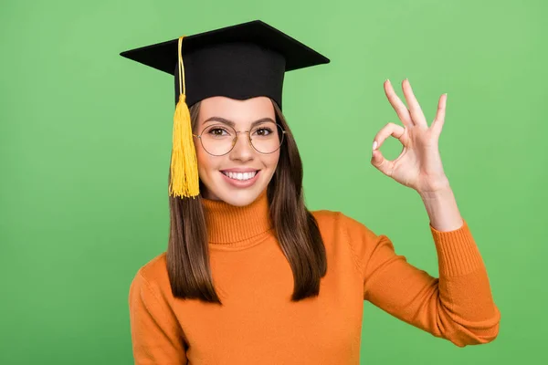 Ritratto di attraente ragazza allegra indossando master cappello mostrando ok-segno laurea isolato su sfondo di colore verde — Foto Stock