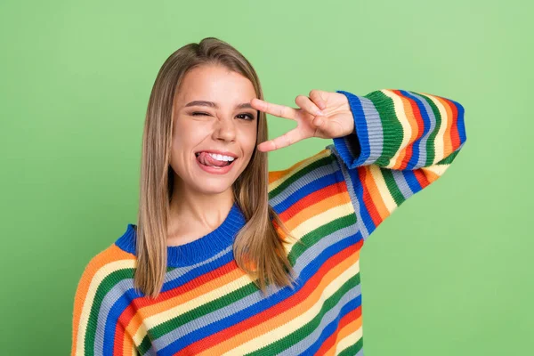 Foto retrato sorridente menina mostrando língua v-sinal gesto vestindo pulôver piscar isolado pastel cor verde fundo — Fotografia de Stock