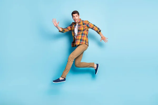 Fénykép elég barátságos fiatal srác öltözött kockás ing mosolygós ugrás magasan futó elszigetelt kék háttér — Stock Fotó