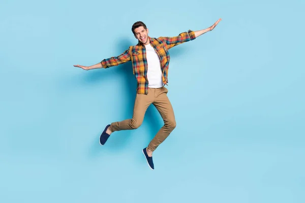 Foto av rolig söt ung kille klädd rutig skjorta glasögon ler hoppa högt isolerad blå färg bakgrund — Stockfoto
