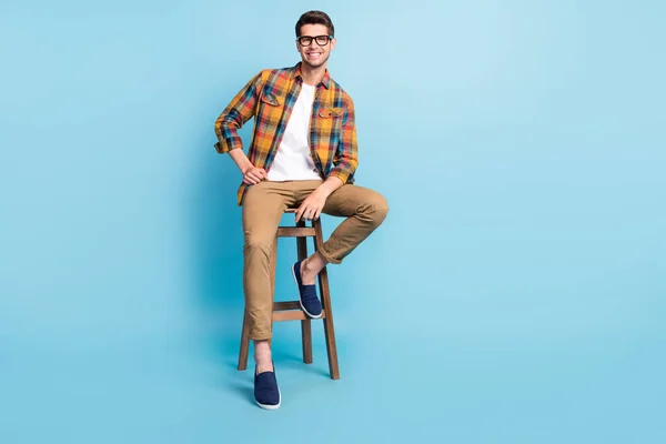 Фото привлекательного милого джентльмена носить клетчатую рубашку руки очки сидя бар стул пустое пространство изолированный синий цвет фона — стоковое фото