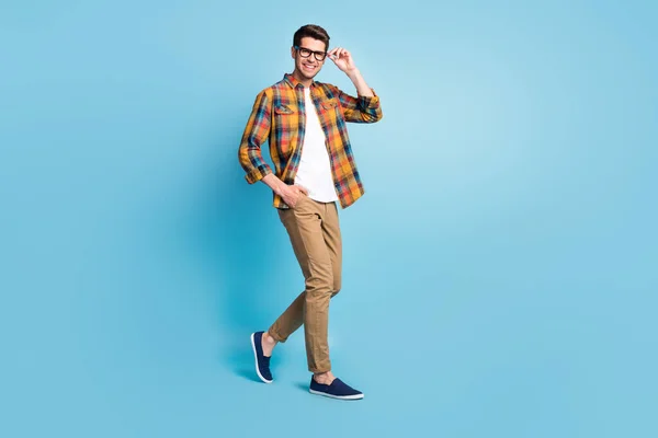 Fotografia dość atrakcyjny młody dżentelmen nosić w kratkę koszula ramię okulary chodzenie uśmiechnięty odizolowany niebieski kolor tło — Zdjęcie stockowe