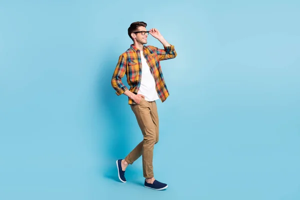 Zdjęcie cute uroczy młody facet ubrany w kratę koszula okulary uśmiechnięty spacery patrząc puste miejsce odizolowane niebieski kolor tło — Zdjęcie stockowe