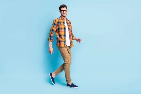 Zdjęcie podekscytowany ładny młody facet ubrany w kratę okulary koszuli uśmiechając się spacery odizolowany niebieski kolor tła — Zdjęcie stockowe