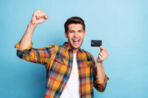 Portret van aantrekkelijke vrolijke man houden in de hand bankkaart vieren met plezier storting geïsoleerd over helder blauwe kleur achtergrond — Stockfoto