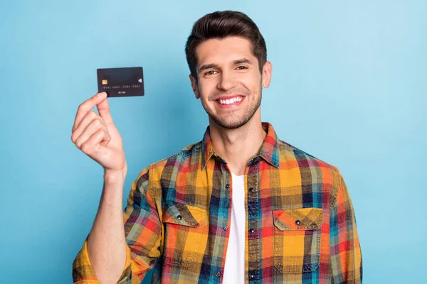 Portret van aantrekkelijke vrolijke man houden in de hand zwarte bankkaart spaardeposito geïsoleerd over helder blauwe kleur achtergrond — Stockfoto