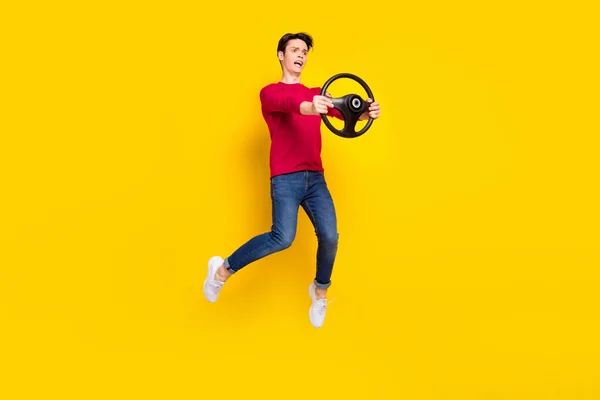 Фотографія повного тіла злий брюнетка тисячолітній хлопець стрибає тримати колесо носити червоний светр джинси ізольовані на жовтому фоні — стокове фото