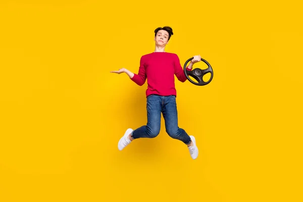 Full size photo of unsure brunet young guy jump hold wheel wear red sweater jeans isolated on yellow color background — Stock Photo, Image