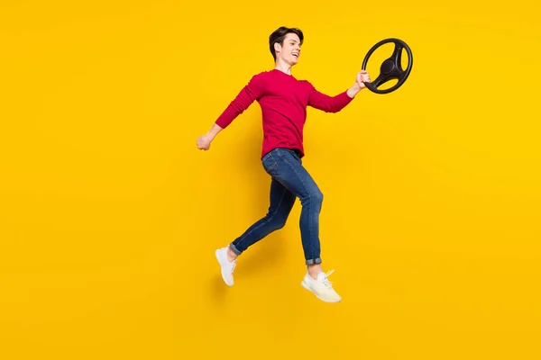 Volledige foto van zoete geschokte jonge heer dragen rode trui springen stuurwiel geïsoleerde gele kleur achtergrond — Stockfoto