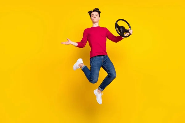 Foto von süßen ernsthaften jungen Herrn tragen roten Pullover springen hoch haltenden Lenkrad isoliert gelbe Farbe Hintergrund — Stockfoto
