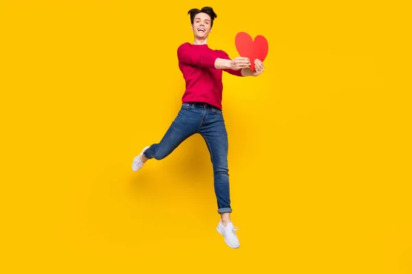 Foto de cuerpo completo de brunet funky millennial chico salto dar corazón desgaste pantalones vaqueros suéter rojo aislado en el fondo de color amarillo —  Fotos de Stock