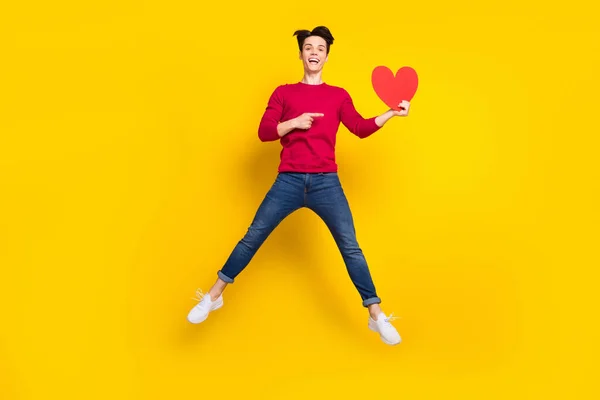 Foto de comprimento total de animado bonito jovem vestido pulôver vermelho apontando dedo vermelho coração pulando isolado cor amarela fundo — Fotografia de Stock