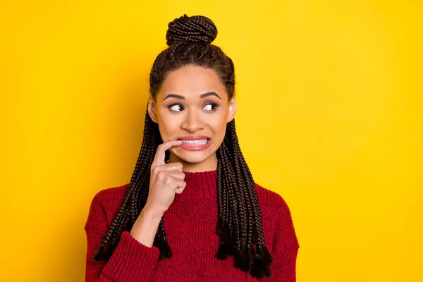 Foto de infeliz culpable piel oscura mujer vestida suéter rojo morder dedo buscando espacio vacío aislado color amarillo fondo — Foto de Stock