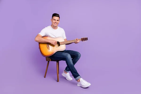 Foto de tamaño completo de hombre alegre feliz positivo sentarse silla jugar guitarra buen humor sonrisa aislada sobre fondo de color violeta — Foto de Stock