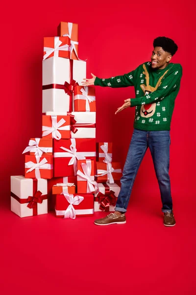 Foto vertical de mãos cara engraçado apresentando grande pilha x-mas giftboxes usar camisola de veado verde isolado no fundo vermelho — Fotografia de Stock