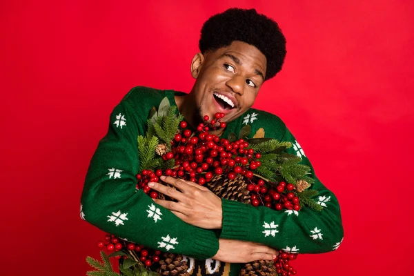Ritratto di attraente ragazzo allegro abbracciando ghirlanda festale Vigilia Noel giorno divertendosi buon umore isolato su sfondo di colore rosso brillante — Foto Stock