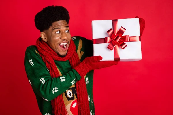 Retrato de chico sorprendido alegre atractivo sosteniendo en mano regalo festal Eve Noel costumbre aislado sobre fondo de color rojo brillante —  Fotos de Stock