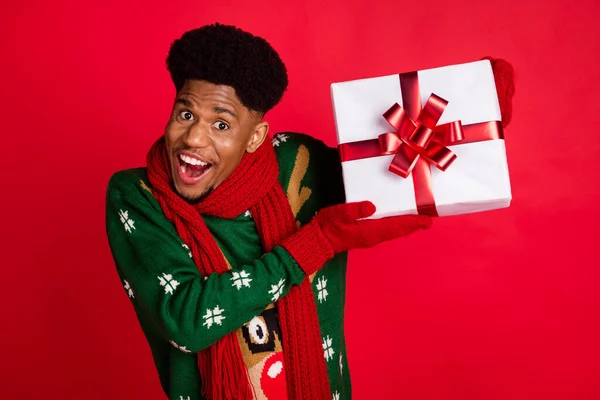 Retrato de chico alegre atractivo sosteniendo en mano regalo caja oferta anuncio Eve Noel aislado sobre fondo de color rojo brillante —  Fotos de Stock