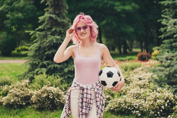 Фото молодой спортивной девушки счастливая положительная улыбка провести футбольный мяч игровой парк Природа рука коснуться солнцезащитных очков на открытом воздухе — стоковое фото