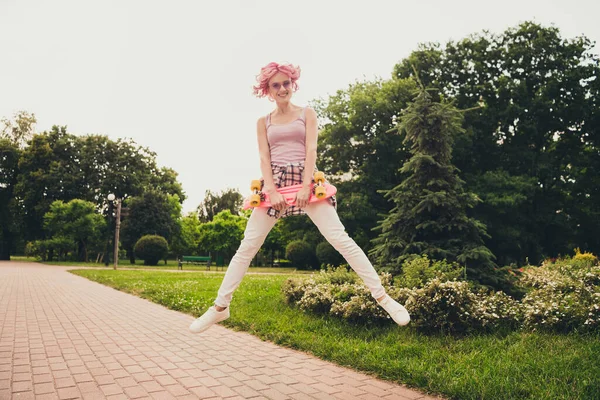 Tamanho do corpo de comprimento total vista de menina alegre atraente pulando passar férias segurando skate no ar fresco viajando ao ar livre — Fotografia de Stock