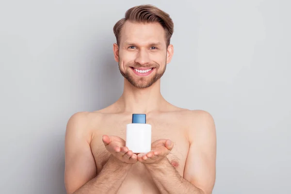 Photo of attractive cheerful blond hair young guy no clothes smiling holding arms balm bottle isolated grey color background — Stock Photo, Image