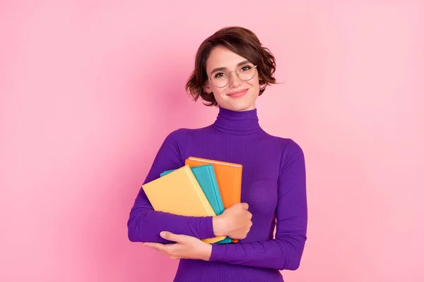 Foto de la joven morena inteligente sostiene libros lleva gafas jersey violeta aislado sobre fondo de color rosa —  Fotos de Stock