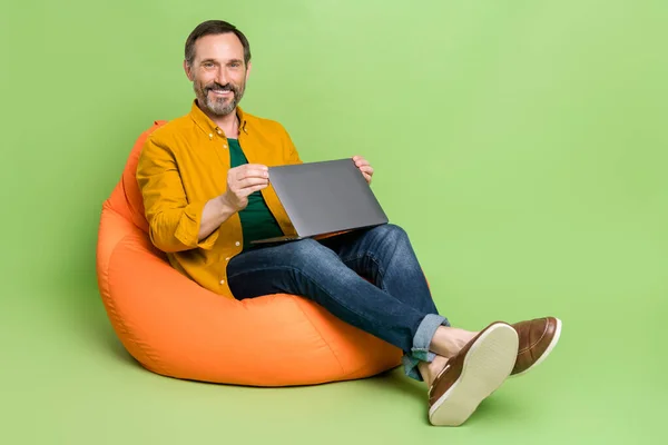 Foto de dulce hombre bastante maduro vestido camisa naranja sentado bolso de frijol trabajando gadget moderno aislado color verde fondo —  Fotos de Stock