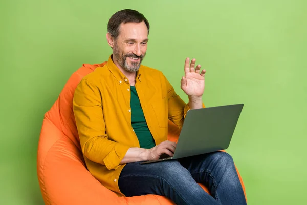 Profile side photo of mature man happy positive smile speak video call laptop chair bean isolated over green color background — Stock Photo, Image