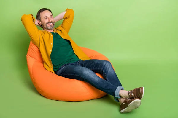 Pleine taille profil côté photo de mature homme heureux sourire positif repos chaise haricot mains derrière la tête isolé sur fond de couleur verte — Photo