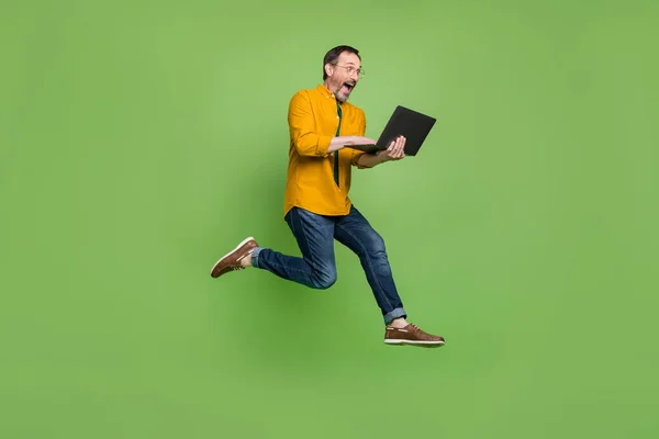 Foto de tamaño completo de pelo castaño feliz hombre sorprendido saltar correr mantenga portátil aislado sobre fondo de color verde —  Fotos de Stock