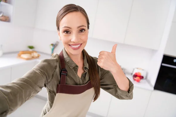 Foto van glimmende schattige huishoudster dragen bruine schort glimlachen tonen duim omhoog opname video binnen kamer huis — Stockfoto