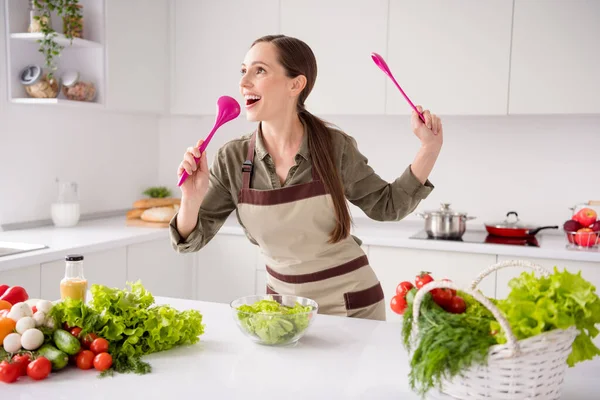 Foto van charmante mooie huisvrouw gekleed bruine schort bereiden smakelijke salade zingen glimlachen binnen huiskamer huis — Stockfoto