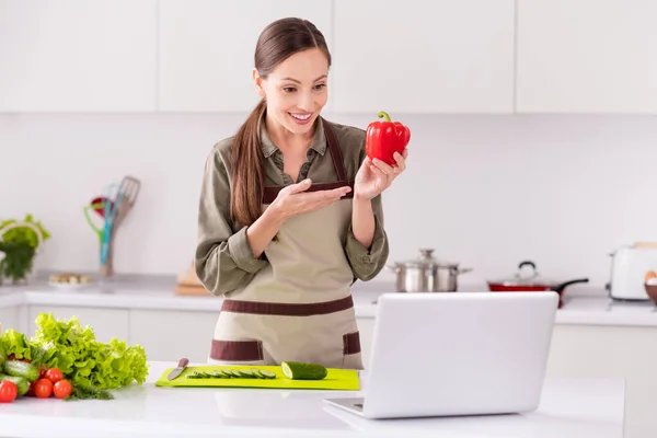 Портрет привабливої веселої жінки, що готує салат з використанням ноутбука, що демонструє процес навчання вдома світло-білий інтер'єр в приміщенні — стокове фото