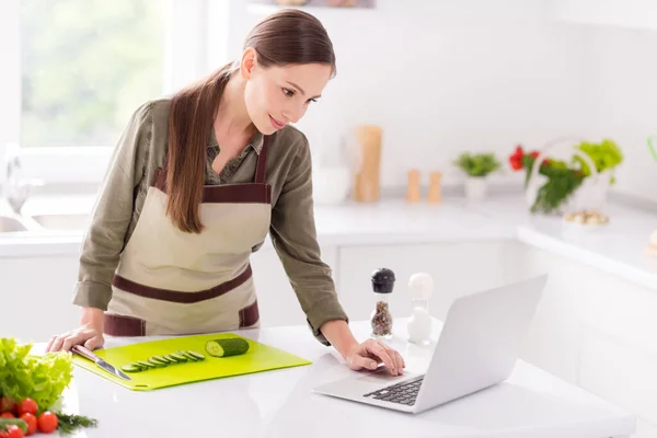 Retrato de mulher atraente preparando salada fresca usando laptop procurando receita em casa luz interior branco dentro de casa — Fotografia de Stock