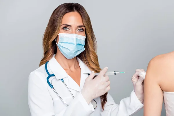 Портрет привабливої жінки-лікаря, що робить ін'єкції антивірус кованого диму ізольовані на сірому пастельному кольоровому фоні — стокове фото