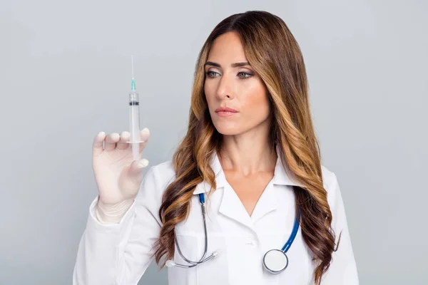 Foto de una joven mujer profesional seria sujeta la aguja de la mano mirada de la vacuna aislada sobre fondo de color gris — Foto de Stock