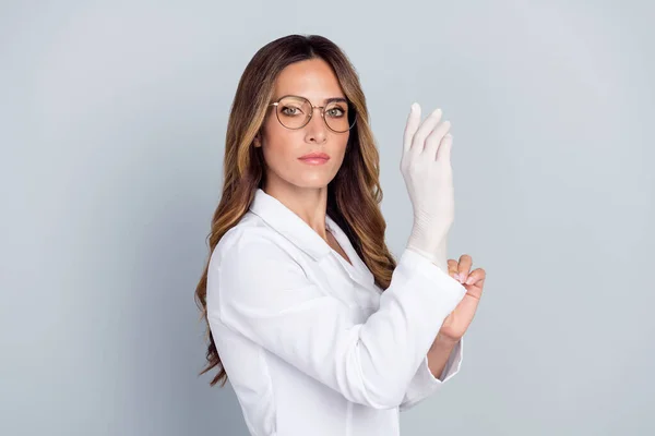 Ritratto di attraente abile donna dai capelli ondulati doc mettendo guanti sulla procedura isolata su sfondo grigio pastello — Foto Stock