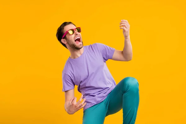 Fénykép a gondatlan rocker srác játszani képzeletbeli gitár sikoly kopás napszemüveg lila póló izolált sárga színű háttér — Stock Fotó