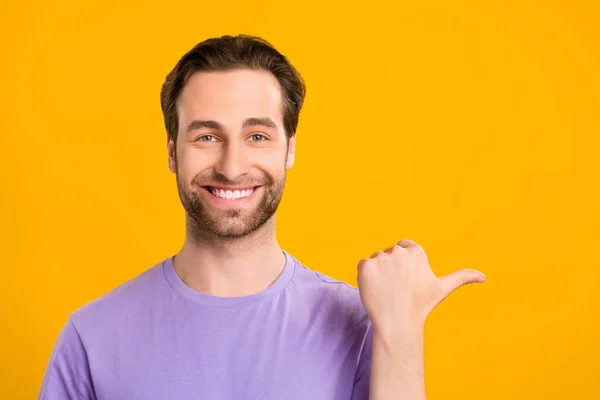 Bild av stilig kille indikerar pekfinger tomt utrymme slitage violett t-shirt isolerad gul färg bakgrund — Stockfoto