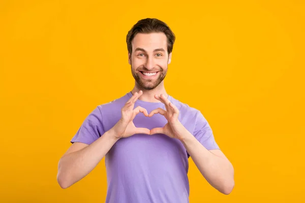 Photo of romantic guy toothy smile show love heart symbol wear purple t-shirt isolated yellow color background — Stock Photo, Image