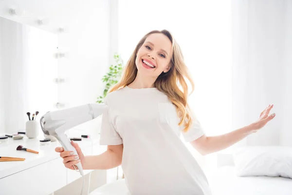 Retrato de atractiva chica rubia alegre y despreocupada secando el cabello teniendo un descanso divertido en el hogar blanco claro en el interior —  Fotos de Stock